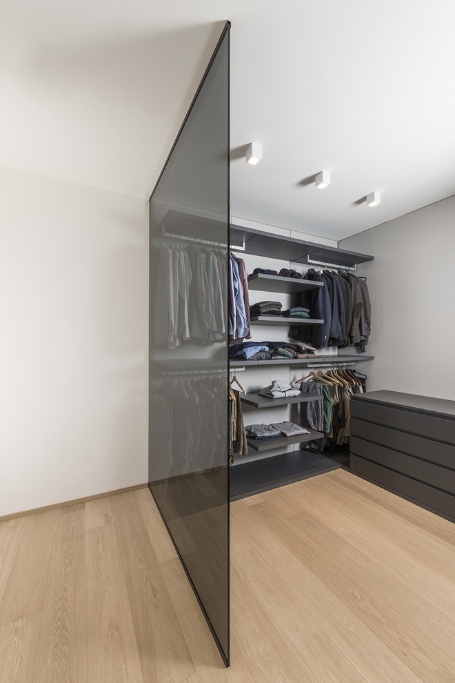 Photo of a mid-sized contemporary men's dressing room in Milan with open cabinets, black cabinets and light hardwood floors.