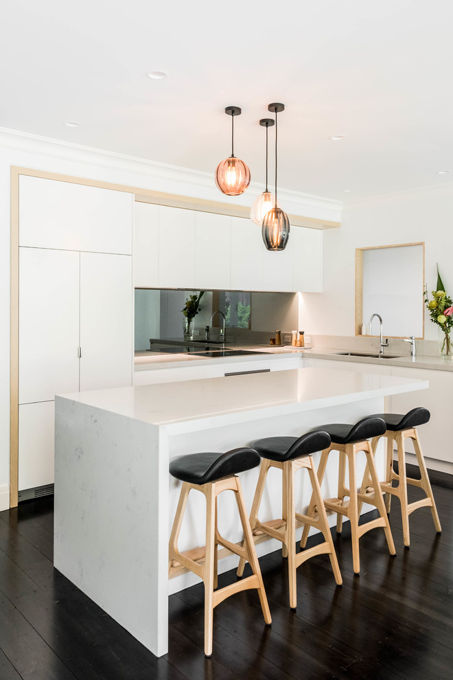 Contemporary l-shaped kitchen in Melbourne with an undermount sink, flat-panel cabinets, white cabinets, metallic splashback, mirror splashback, panelled appliances, painted wood floors, with island, black floor and white benchtop.