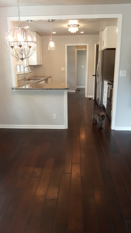 Example of a mid-sized transitional galley dark wood floor open concept kitchen design with an undermount sink, shaker cabinets, white cabinets, granite countertops, white backsplash, stainless steel appliances and a peninsula