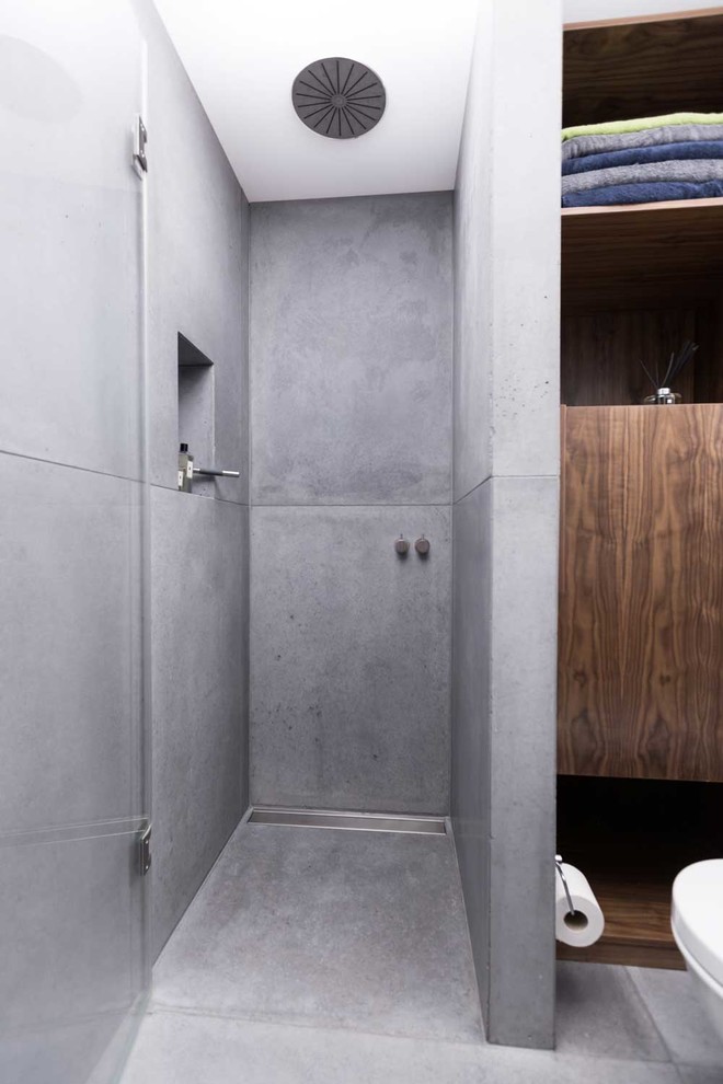 This is an example of a mid-sized contemporary 3/4 bathroom in London with a vessel sink, open cabinets, dark wood cabinets, wood benchtops, a curbless shower, a wall-mount toilet, gray tile, cement tile, grey walls and concrete floors.