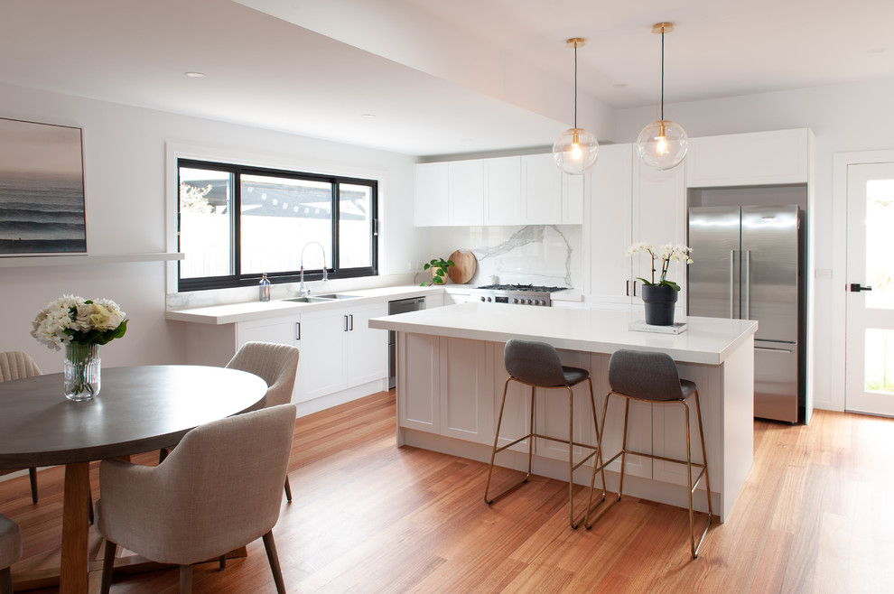 Design ideas for a large transitional u-shaped kitchen pantry in Melbourne with an undermount sink, recessed-panel cabinets, white cabinets, white splashback, stone slab splashback, stainless steel appliances, medium hardwood floors, with island and white benchtop.