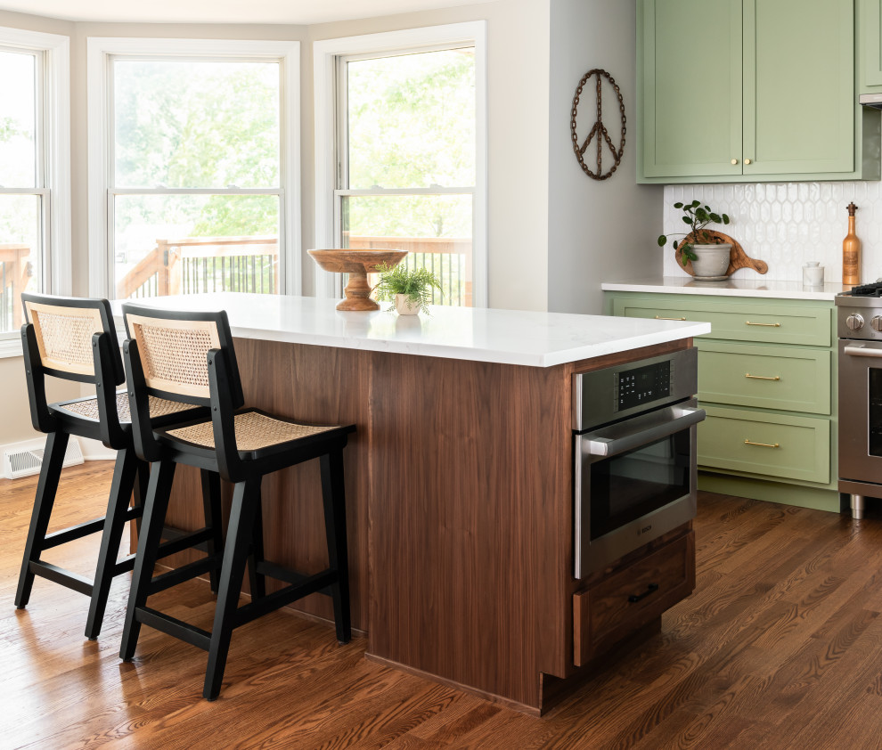 Inspiration for a mid-sized midcentury l-shaped eat-in kitchen in St Louis with an undermount sink, shaker cabinets, green cabinets, quartz benchtops, white splashback, ceramic splashback, stainless steel appliances, light hardwood floors, with island, brown floor and white benchtop.