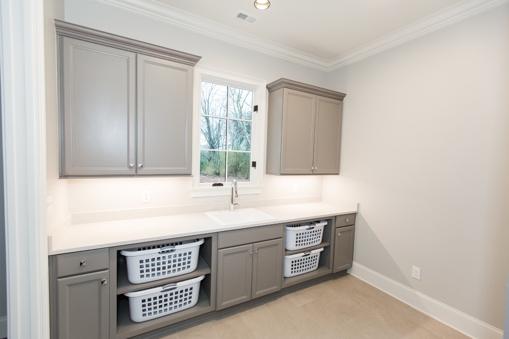 Photo of a mid-sized contemporary galley dedicated laundry room in Birmingham with a drop-in sink, recessed-panel cabinets, grey cabinets, solid surface benchtops, white walls, beige floor and beige benchtop.
