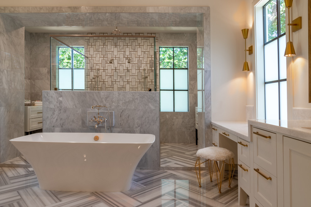 Large transitional master bathroom in Houston with recessed-panel cabinets, white cabinets, a freestanding tub, a double shower, gray tile, white tile, limestone, white walls, limestone floors, an undermount sink, solid surface benchtops, white floor, a hinged shower door and white benchtops.
