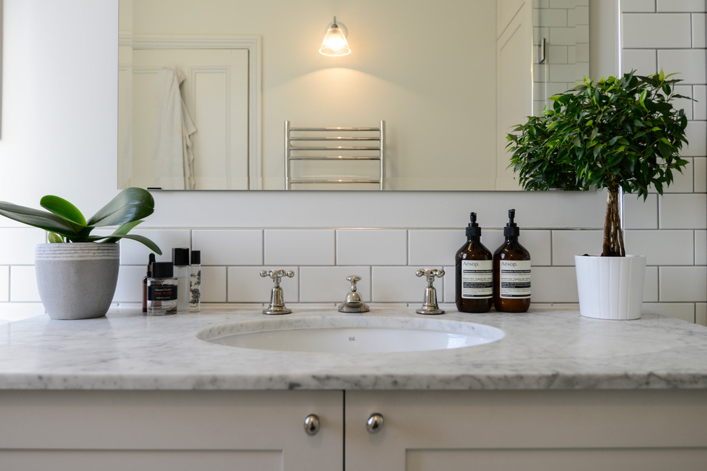 Photo of a transitional bathroom in London with an undermount sink, a one-piece toilet, white cabinets, marble benchtops, white tile and subway tile.
