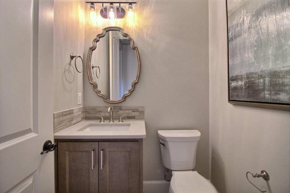 Design ideas for a mid-sized arts and crafts powder room in Portland with recessed-panel cabinets, dark wood cabinets, a two-piece toilet, multi-coloured tile, ceramic tile, grey walls, ceramic floors, an undermount sink, engineered quartz benchtops, grey floor and white benchtops.