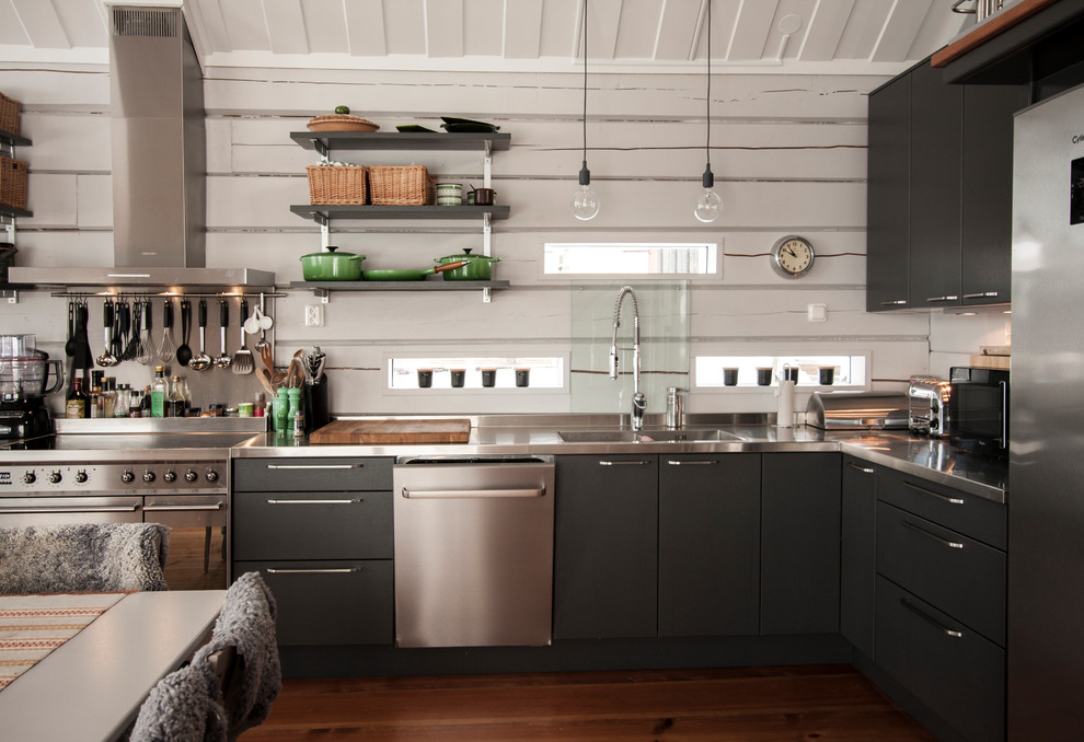 Inspiration for a mid-sized industrial l-shaped eat-in kitchen in Gothenburg with a double-bowl sink, flat-panel cabinets, black cabinets, stainless steel benchtops, stainless steel appliances and medium hardwood floors.