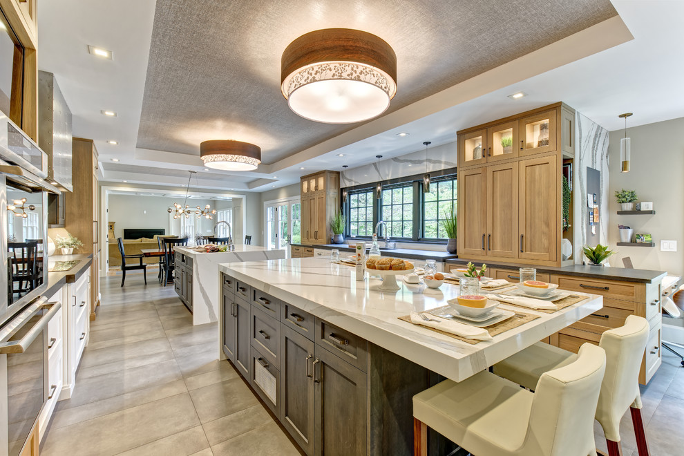 Large transitional galley eat-in kitchen in New York with an undermount sink, shaker cabinets, grey cabinets, quartz benchtops, white splashback, stone slab splashback, stainless steel appliances, porcelain floors, multiple islands, grey floor and white benchtop.