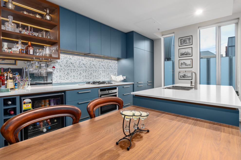 Bild på ett stort funkis vit vitt kök, med en undermonterad diskho, släta luckor, blå skåp, bänkskiva i kvarts, blått stänkskydd, stänkskydd i porslinskakel, svarta vitvaror, klinkergolv i porslin, flera köksöar och grått golv
