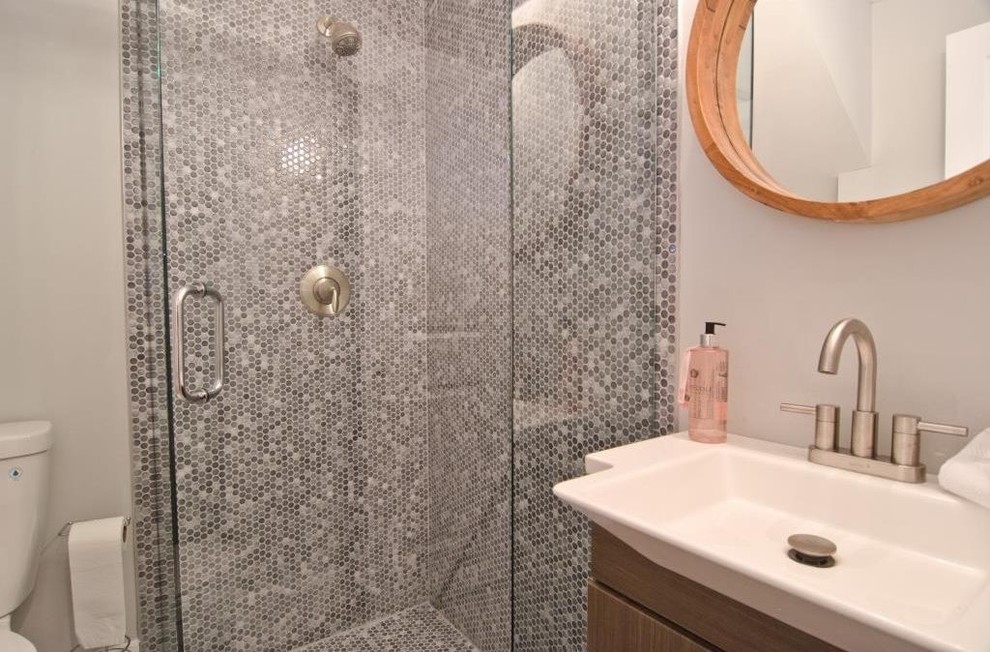 This is an example of a small contemporary 3/4 bathroom in Miami with flat-panel cabinets, dark wood cabinets, a corner shower, a one-piece toilet, gray tile, grey walls, an integrated sink and a hinged shower door.