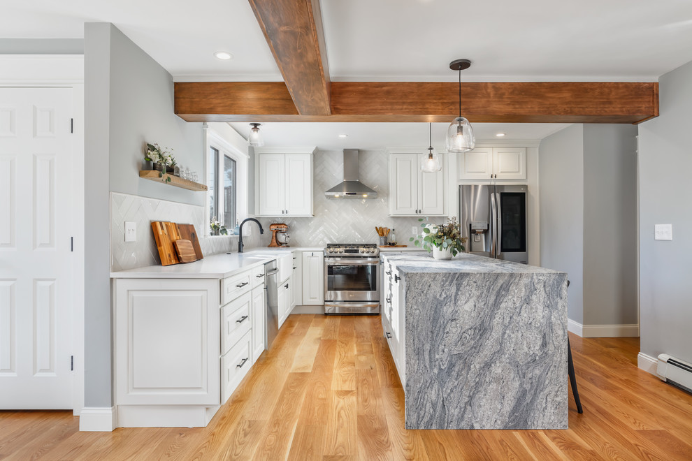 Photo of a mid-sized transitional l-shaped eat-in kitchen in Boston with a farmhouse sink, raised-panel cabinets, white cabinets, quartz benchtops, white splashback, subway tile splashback, stainless steel appliances, light hardwood floors, with island, beige floor and white benchtop.