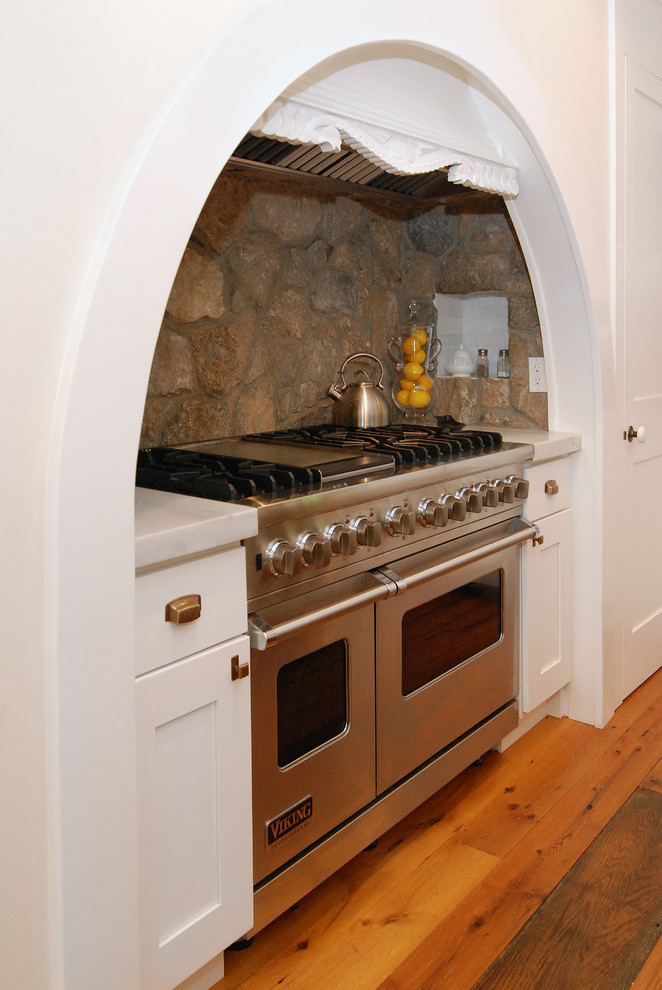 This is an example of a large country l-shaped kitchen in New York with stainless steel appliances, recessed-panel cabinets, white cabinets, grey splashback, a drop-in sink, medium hardwood floors and with island.