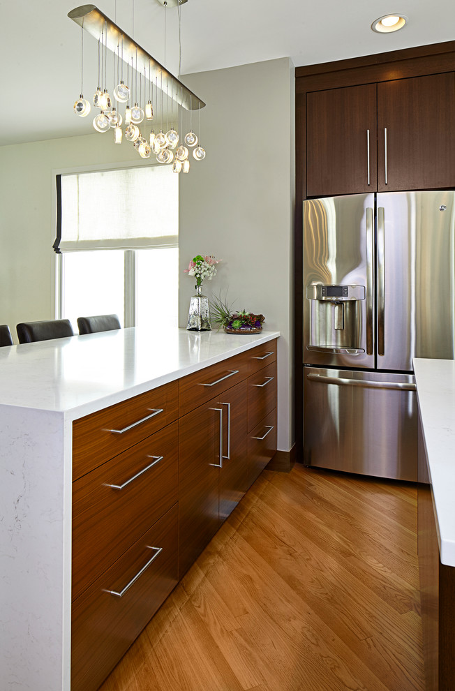 Photo of a small eclectic u-shaped eat-in kitchen in Chicago with an undermount sink, flat-panel cabinets, brown cabinets, quartz benchtops, white splashback, glass tile splashback, stainless steel appliances, light hardwood floors and with island.