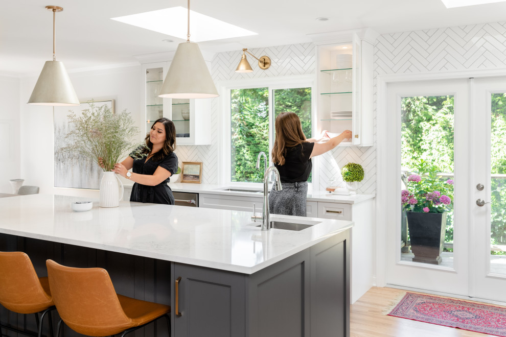 Inspiration for a large transitional l-shaped light wood floor and beige floor open concept kitchen remodel in Vancouver with an undermount sink, recessed-panel cabinets, white cabinets, quartz countertops, white backsplash, ceramic backsplash, stainless steel appliances, an island and white countertops