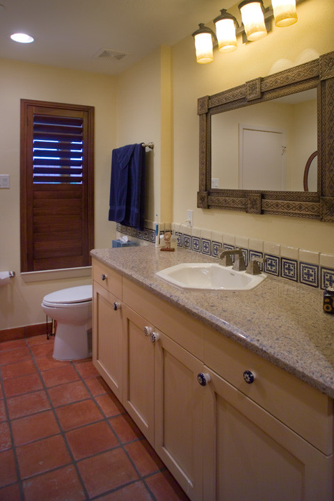 Photo of a mid-sized country 3/4 bathroom in Houston with an integrated sink, recessed-panel cabinets, light wood cabinets, granite benchtops, a drop-in tub, a shower/bathtub combo, a two-piece toilet, blue tile, stone tile, beige walls and terra-cotta floors.
