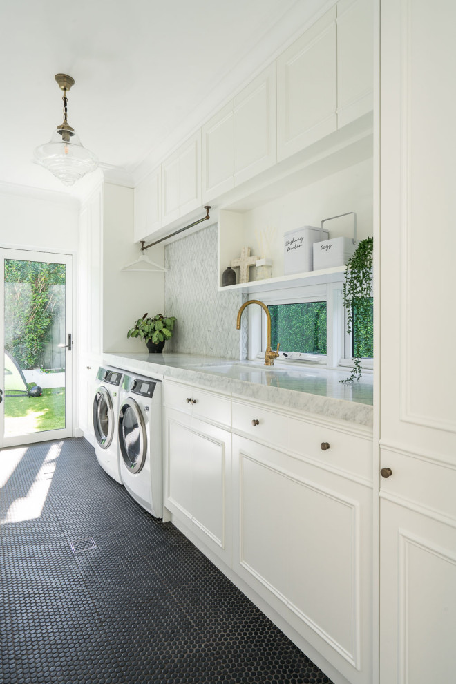 Photo of a transitional single-wall laundry room in Sydney with an undermount sink, recessed-panel cabinets, white cabinets, white walls, a side-by-side washer and dryer, black floor and grey benchtop.