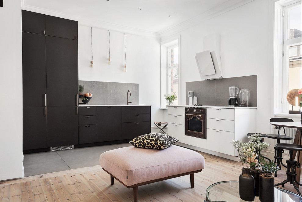 Design ideas for a mid-sized scandinavian l-shaped open plan kitchen in Stockholm with flat-panel cabinets, black cabinets, grey splashback, black appliances, light hardwood floors and no island.