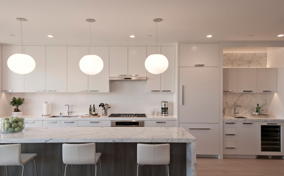 Design ideas for a large contemporary single-wall open plan kitchen in San Francisco with an undermount sink, flat-panel cabinets, white cabinets, marble benchtops, white splashback, stone slab splashback, panelled appliances, light hardwood floors and with island.