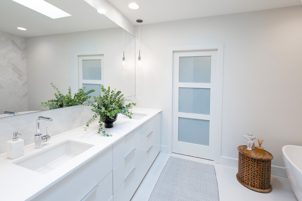 Photo of a mid-sized transitional master bathroom in Denver with a one-piece toilet, white walls, porcelain floors, an undermount sink, white floor, flat-panel cabinets, white cabinets, solid surface benchtops, white benchtops, a freestanding tub, a corner shower, marble and a hinged shower door.