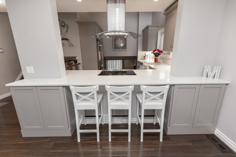 Example of a transitional dark wood floor and brown floor eat-in kitchen design in Calgary with shaker cabinets, gray cabinets, quartz countertops, white backsplash and stainless steel appliances