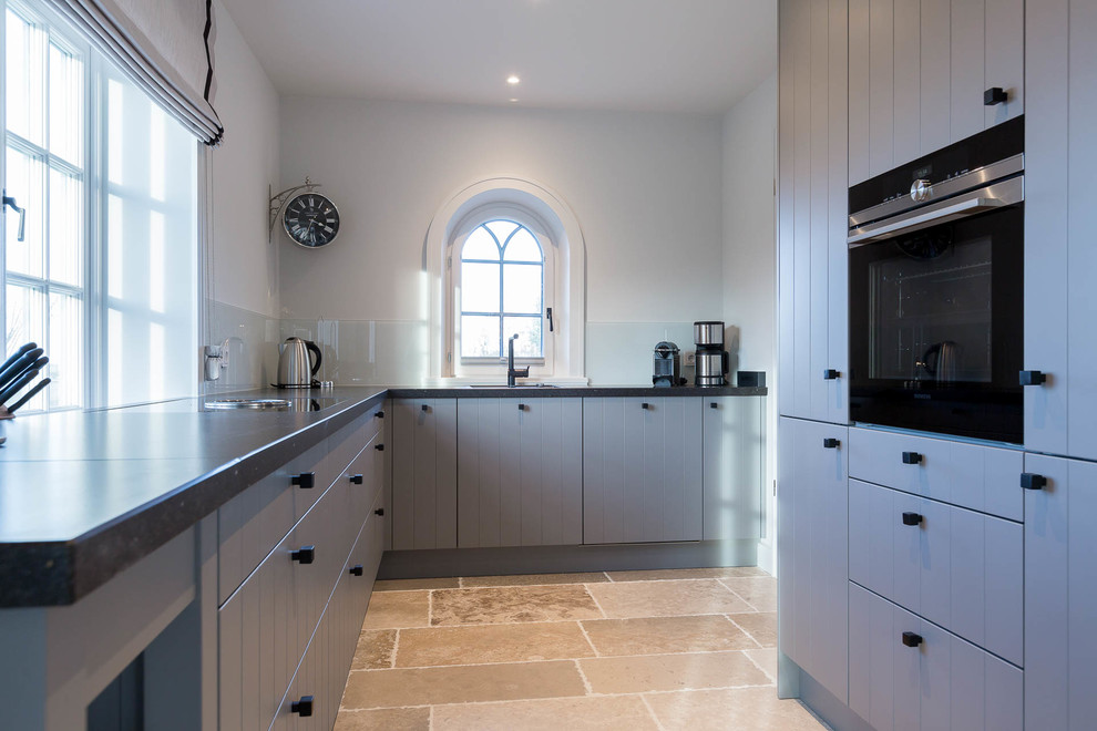 Inspiration for a mid-sized country l-shaped open plan kitchen in Other with a drop-in sink, louvered cabinets, blue cabinets, white splashback, glass sheet splashback, black appliances, slate floors, no island, beige floor and black benchtop.