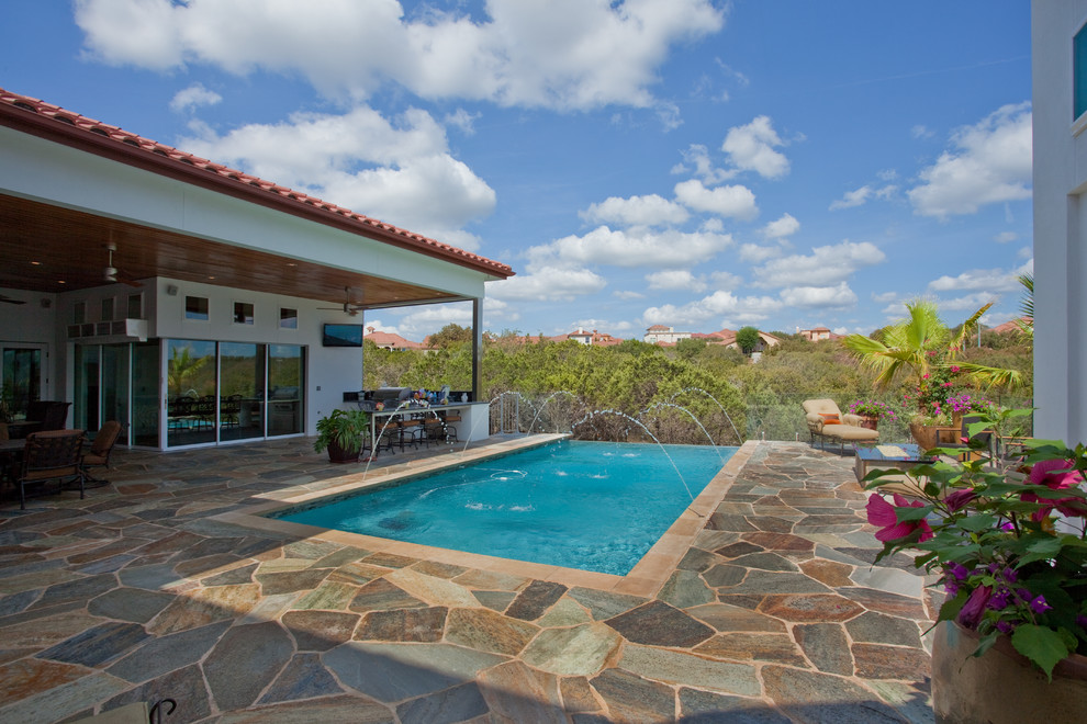Mid-sized country backyard rectangular infinity pool in Austin with natural stone pavers.