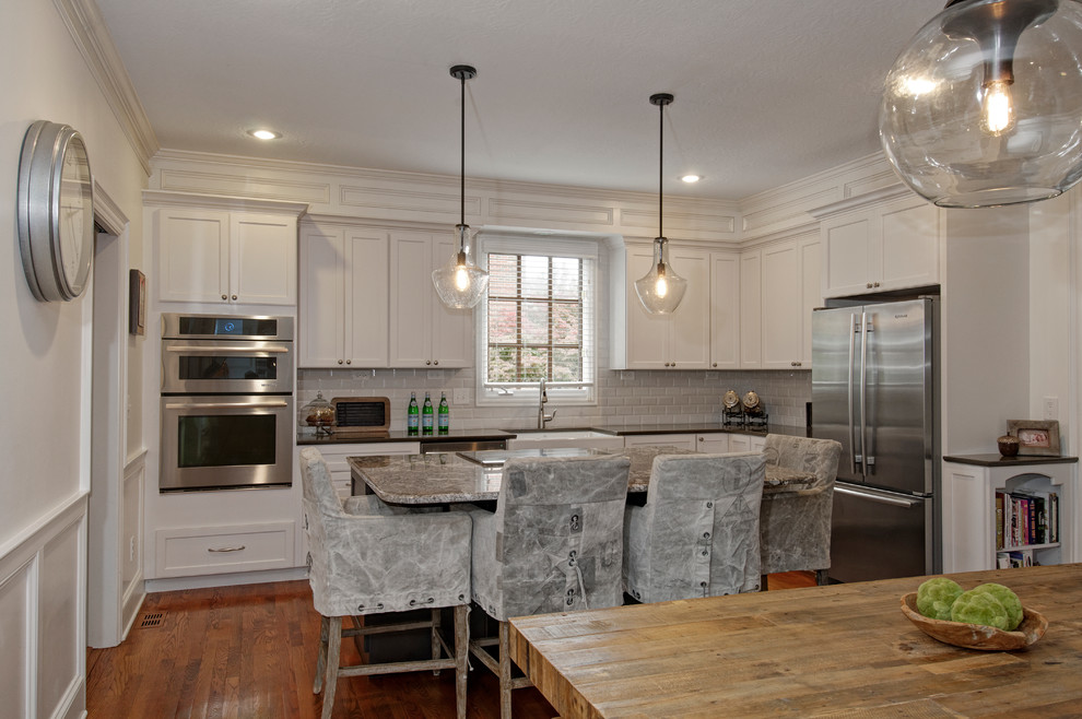 Inspiration for a mid-sized kitchen in Columbus with a farmhouse sink, flat-panel cabinets, quartz benchtops, white splashback, stainless steel appliances, light hardwood floors and with island.