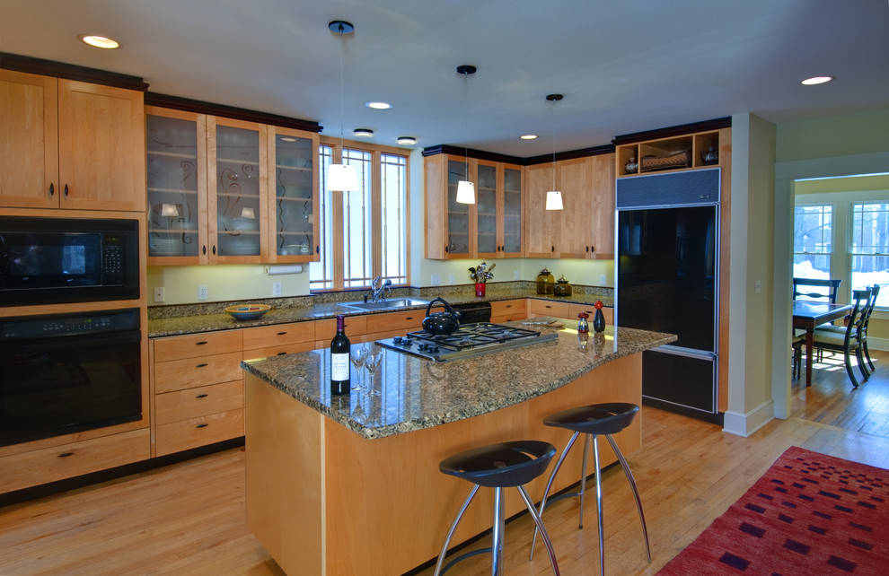 This is an example of a mid-sized eclectic kitchen in Detroit with an undermount sink, shaker cabinets, light wood cabinets, granite benchtops, black appliances, light hardwood floors and with island.