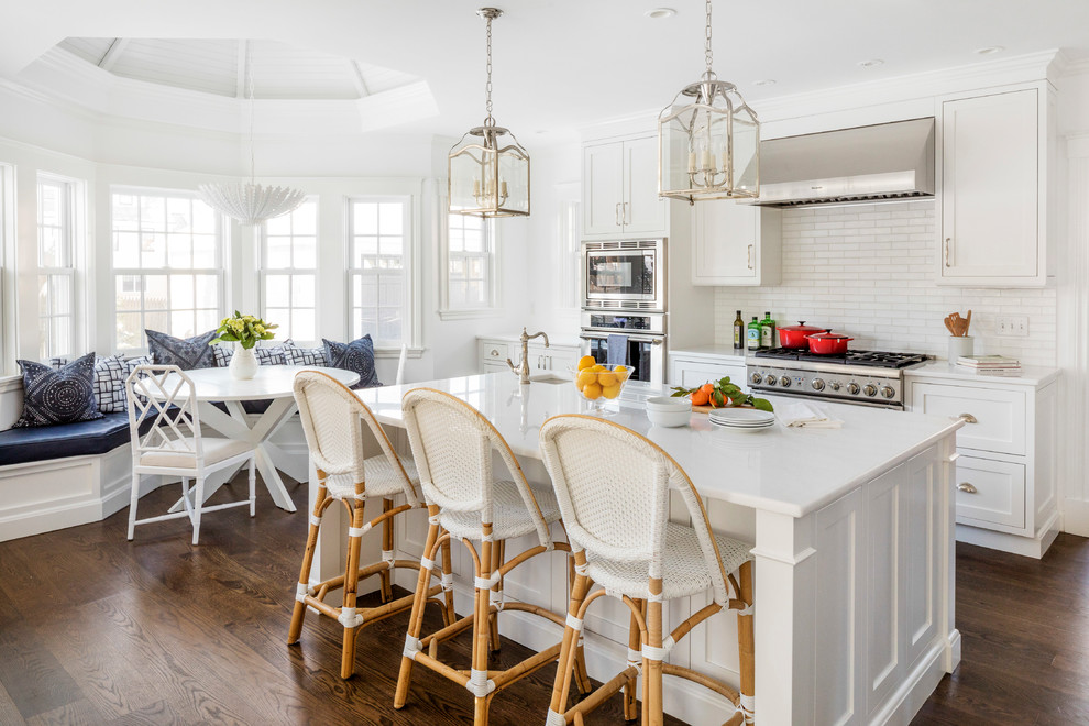 Large transitional eat-in kitchen in Boston with white cabinets, solid surface benchtops, white splashback, ceramic splashback, stainless steel appliances, dark hardwood floors, with island, brown floor, white benchtop and shaker cabinets.