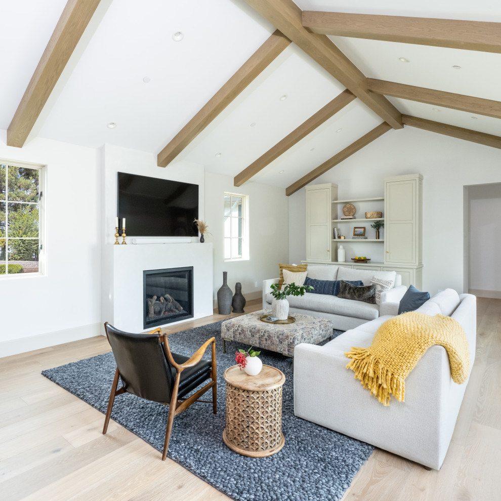 Inspiration for a large transitional open concept living room in San Francisco with white walls, light hardwood floors, a standard fireplace, a plaster fireplace surround, a wall-mounted tv, exposed beam, vaulted and beige floor.
