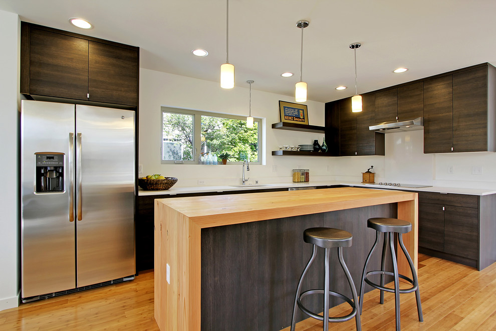 Inspiration for a contemporary l-shaped kitchen in Seattle with flat-panel cabinets, stainless steel appliances, white splashback, dark wood cabinets and wood benchtops.