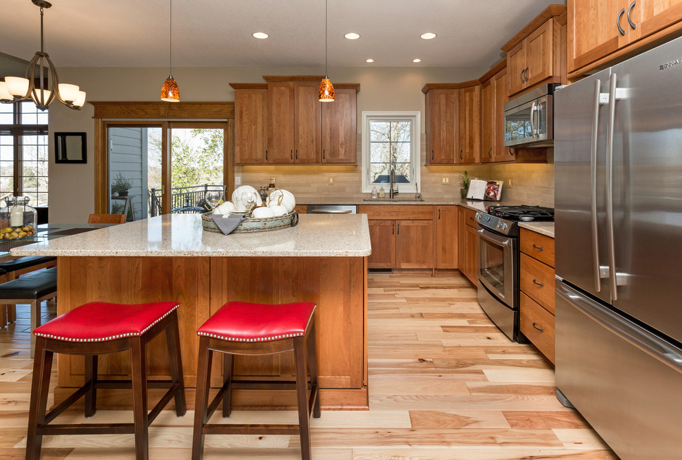 Example of a mid-sized transitional l-shaped light wood floor open concept kitchen design with an undermount sink, recessed-panel cabinets, medium tone wood cabinets, quartz countertops, beige backsplash, stone tile backsplash, stainless steel appliances and an island