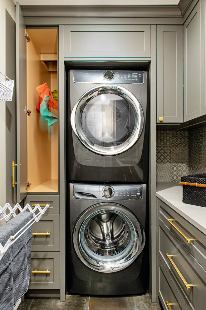 Small transitional l-shaped laundry room in Toronto with an undermount sink, shaker cabinets, grey cabinets, quartz benchtops, grey splashback, ceramic splashback, grey walls, ceramic floors, a stacked washer and dryer, black floor and grey benchtop.