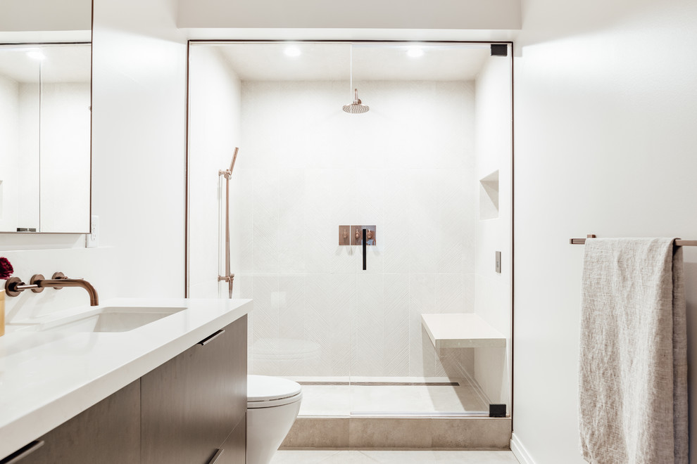 Design ideas for a mid-sized mediterranean master bathroom in Salt Lake City with flat-panel cabinets, dark wood cabinets, a one-piece toilet, beige tile, ceramic tile, white walls, ceramic floors, an integrated sink, solid surface benchtops, beige floor and beige benchtops.