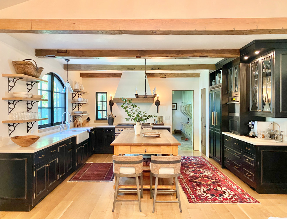 Large scandinavian u-shaped open plan kitchen in Denver with a farmhouse sink, flat-panel cabinets, black cabinets, concrete benchtops, panelled appliances, light hardwood floors, with island, white benchtop and exposed beam.