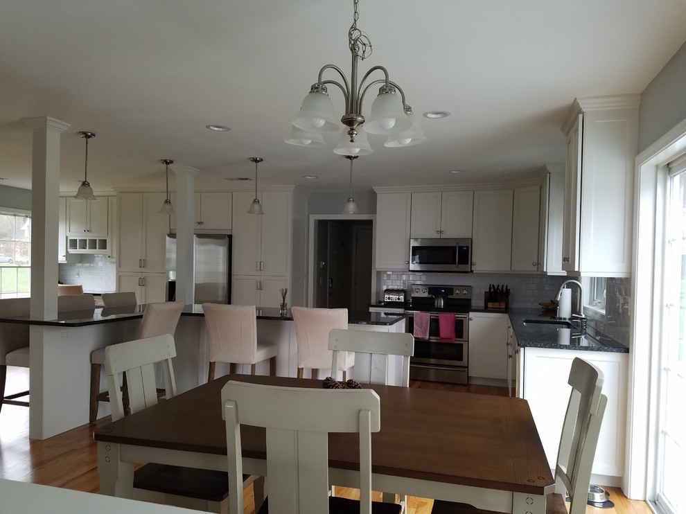 Example of a large transitional l-shaped light wood floor and brown floor eat-in kitchen design with an undermount sink, shaker cabinets, white cabinets, granite countertops, white backsplash, subway tile backsplash, stainless steel appliances and an island