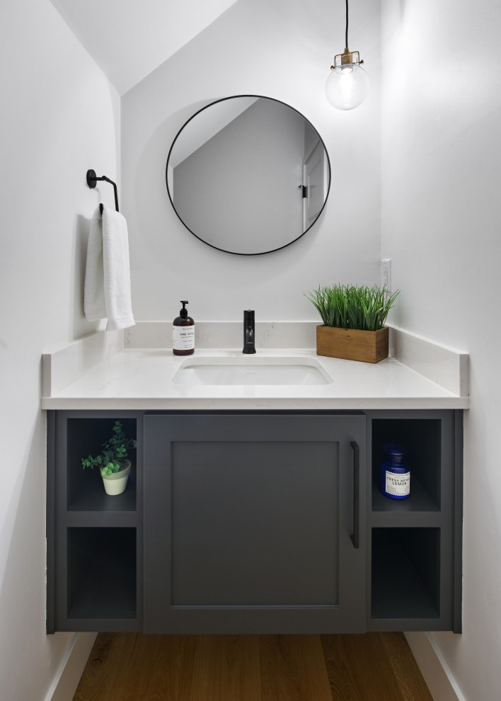 Small country powder room in Other with shaker cabinets, grey cabinets, a one-piece toilet, white walls, light hardwood floors, an undermount sink, engineered quartz benchtops, brown floor, white benchtops and a floating vanity.