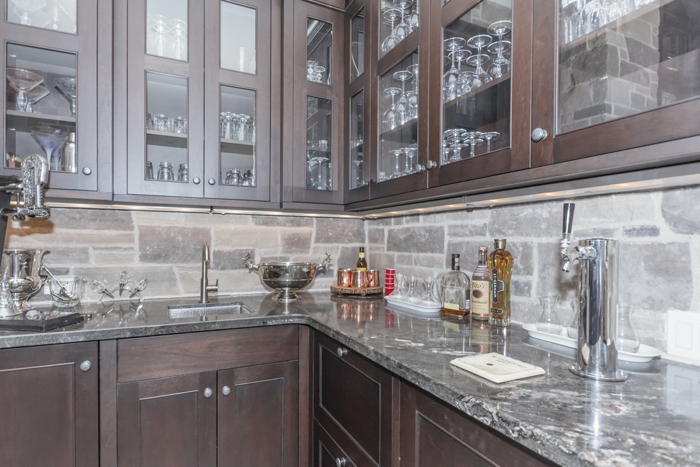 Expansive traditional l-shaped home bar in Toronto with glass-front cabinets, granite benchtops, an undermount sink, medium wood cabinets and stone tile splashback.