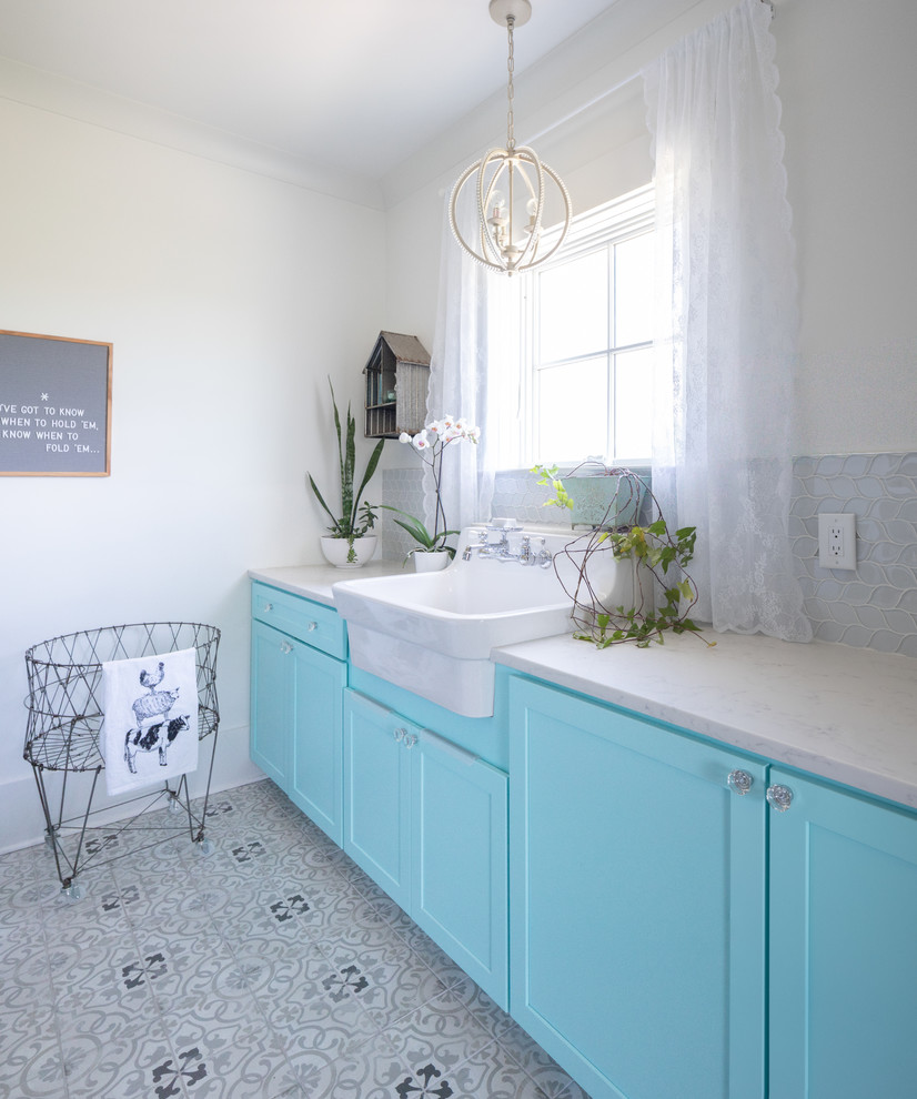 This is an example of a mid-sized country single-wall dedicated laundry room in Nashville with a farmhouse sink, shaker cabinets, blue cabinets, quartz benchtops, white walls, ceramic floors, a side-by-side washer and dryer, grey floor and white benchtop.