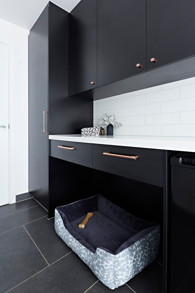 Inspiration for a mid-sized modern single-wall dedicated laundry room in Melbourne with an undermount sink, black cabinets, a stacked washer and dryer, black floor, white benchtop, quartz benchtops and white walls.