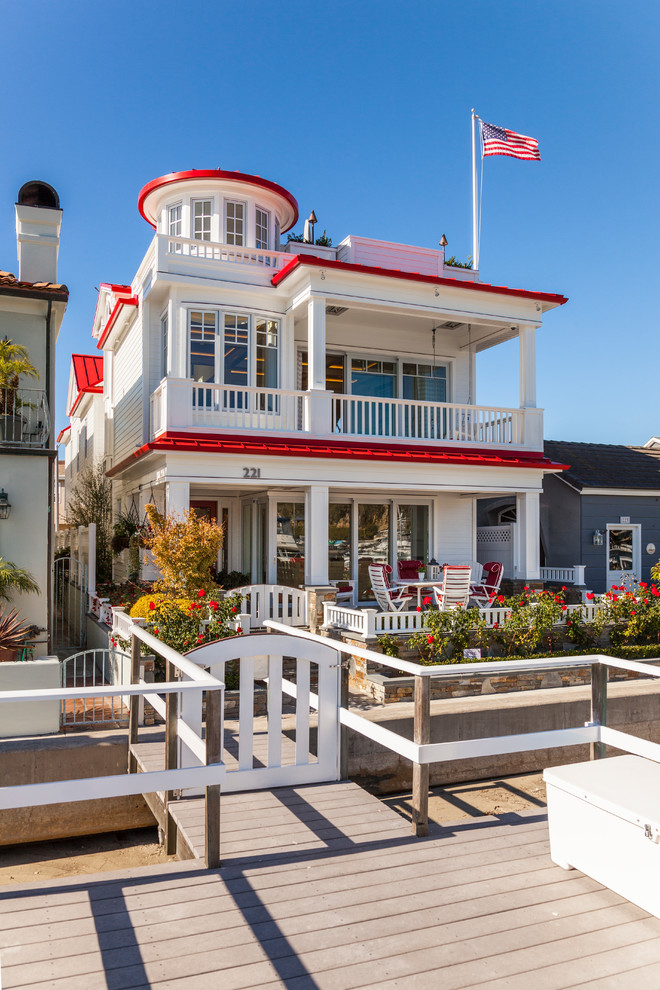 Design ideas for a beach style three-storey white exterior in Orange County with a red roof.