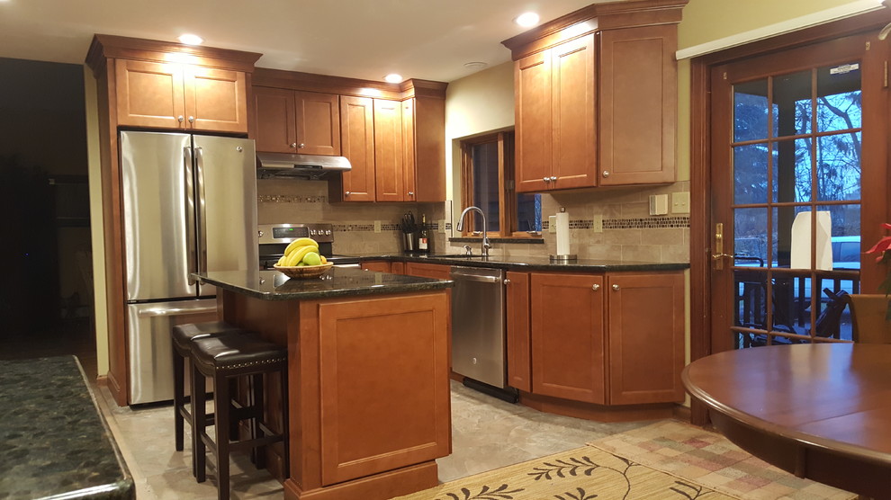 Photo of a mid-sized traditional l-shaped eat-in kitchen in Boston with an undermount sink, recessed-panel cabinets, dark wood cabinets, quartz benchtops, beige splashback, ceramic splashback, stainless steel appliances, ceramic floors, with island, beige floor and black benchtop.