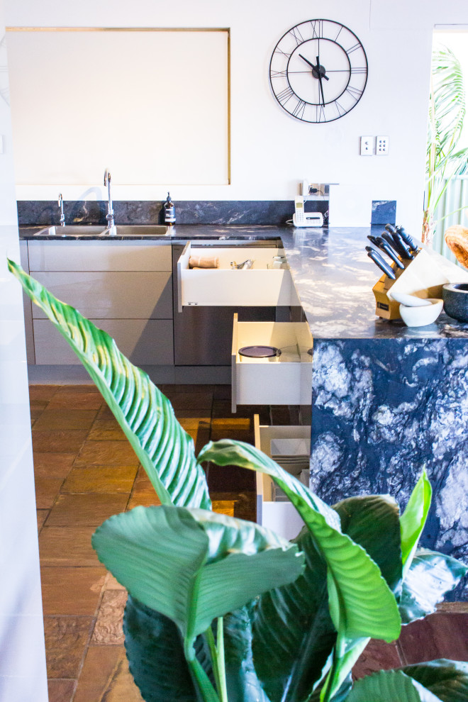 Inspiration for a large modern u-shaped kitchen pantry in Central Coast with a double-bowl sink, flat-panel cabinets, beige cabinets, granite benchtops, metallic splashback, glass sheet splashback, stainless steel appliances, slate floors, a peninsula, brown floor and black benchtop.