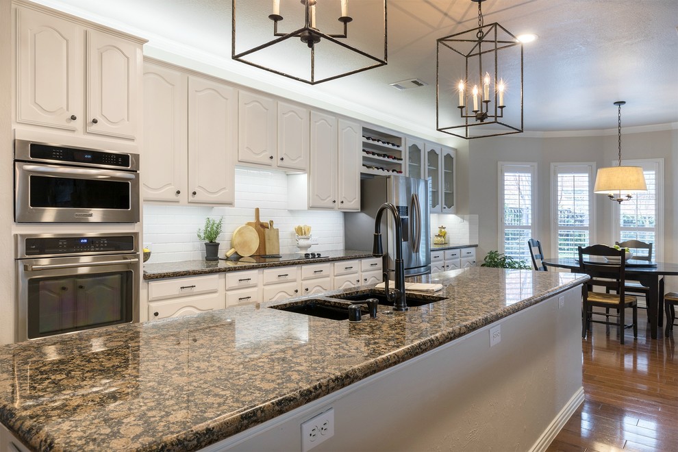 Open concept kitchen - large transitional galley medium tone wood floor open concept kitchen idea in Dallas with an undermount sink, white cabinets, granite countertops, white backsplash, subway tile backsplash, stainless steel appliances and two islands