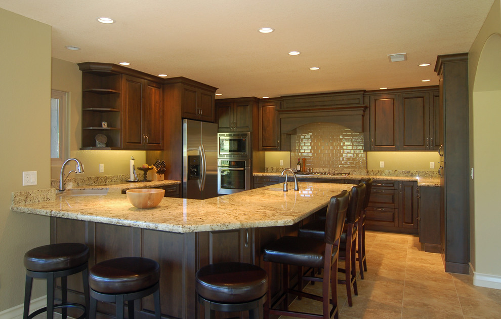 This is an example of an expansive traditional u-shaped eat-in kitchen in San Luis Obispo with an undermount sink, raised-panel cabinets, dark wood cabinets, granite benchtops, green splashback, glass tile splashback, stainless steel appliances, ceramic floors and a peninsula.