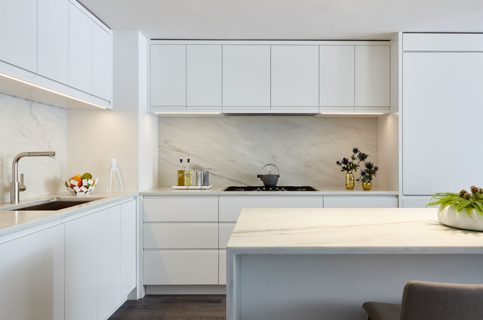 This is an example of a mid-sized modern l-shaped open plan kitchen in New York with an undermount sink, flat-panel cabinets, white cabinets, marble benchtops, multi-coloured splashback, stone slab splashback, white appliances, medium hardwood floors, with island, brown floor and multi-coloured benchtop.