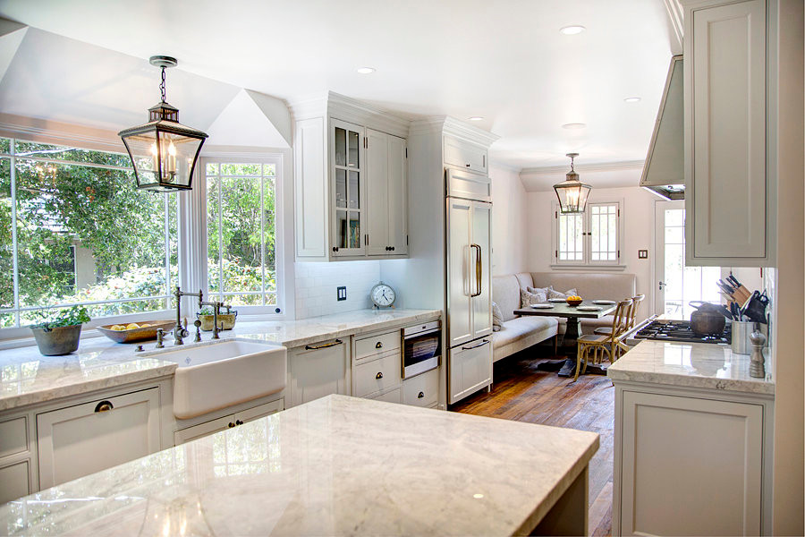 Design ideas for a large traditional galley eat-in kitchen in Los Angeles with a farmhouse sink, glass-front cabinets, white cabinets, quartzite benchtops, white splashback, porcelain splashback, panelled appliances, medium hardwood floors and with island.