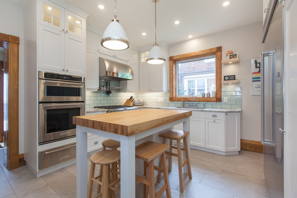 Transitional l-shaped gray floor enclosed kitchen photo in Toronto with shaker cabinets, white cabinets, wood countertops, green backsplash, subway tile backsplash, stainless steel appliances and an island
