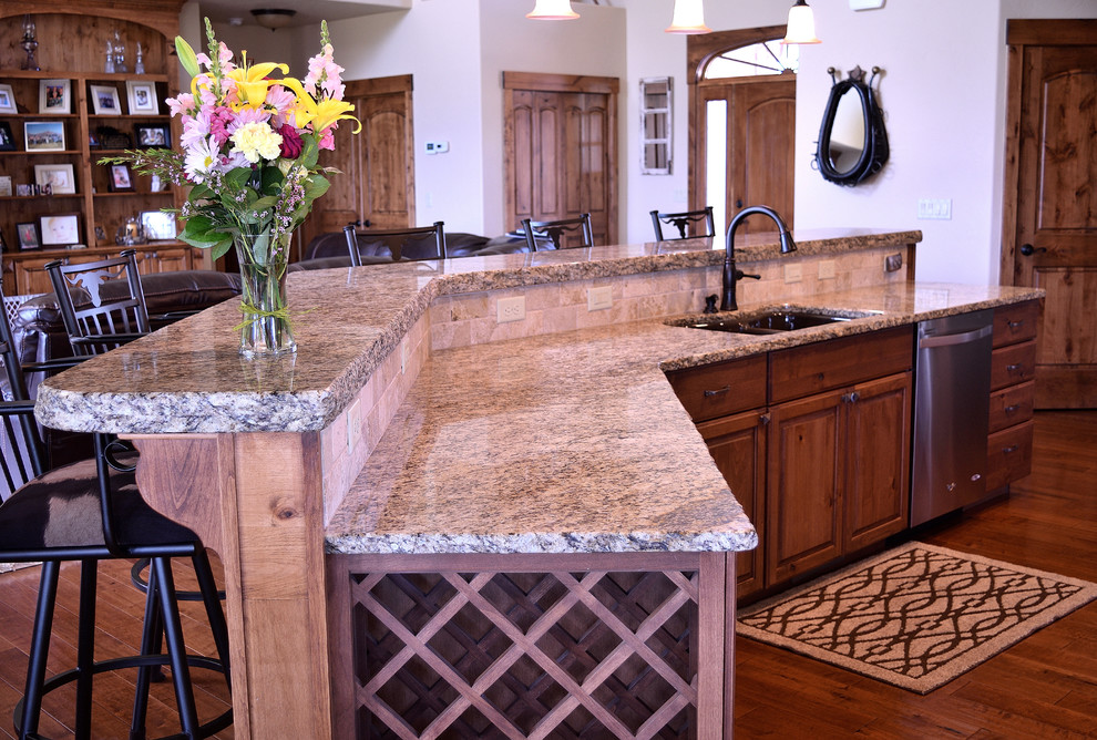 Inspiration for a large rustic galley medium tone wood floor and brown floor eat-in kitchen remodel in Denver with an undermount sink, medium tone wood cabinets, granite countertops, beige backsplash, stone tile backsplash, stainless steel appliances, an island and raised-panel cabinets