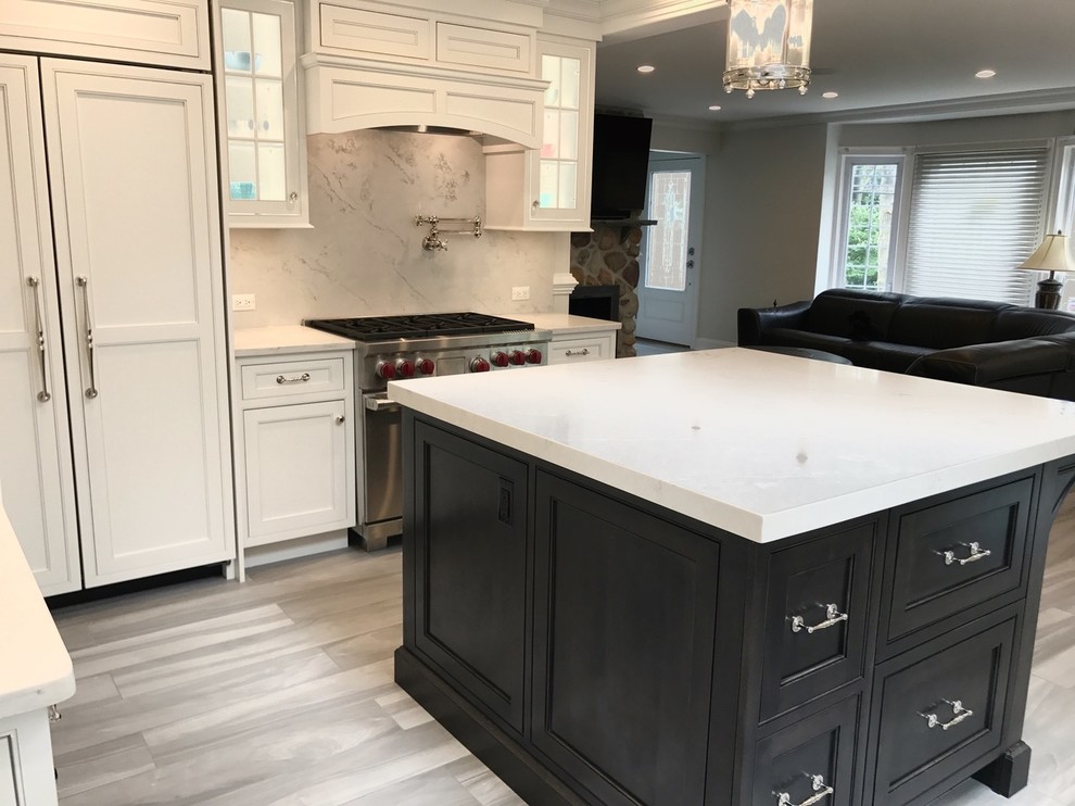 Example of a mid-sized transitional u-shaped light wood floor and brown floor open concept kitchen design with a farmhouse sink, recessed-panel cabinets, white cabinets, marble countertops, white backsplash, marble backsplash, stainless steel appliances and an island